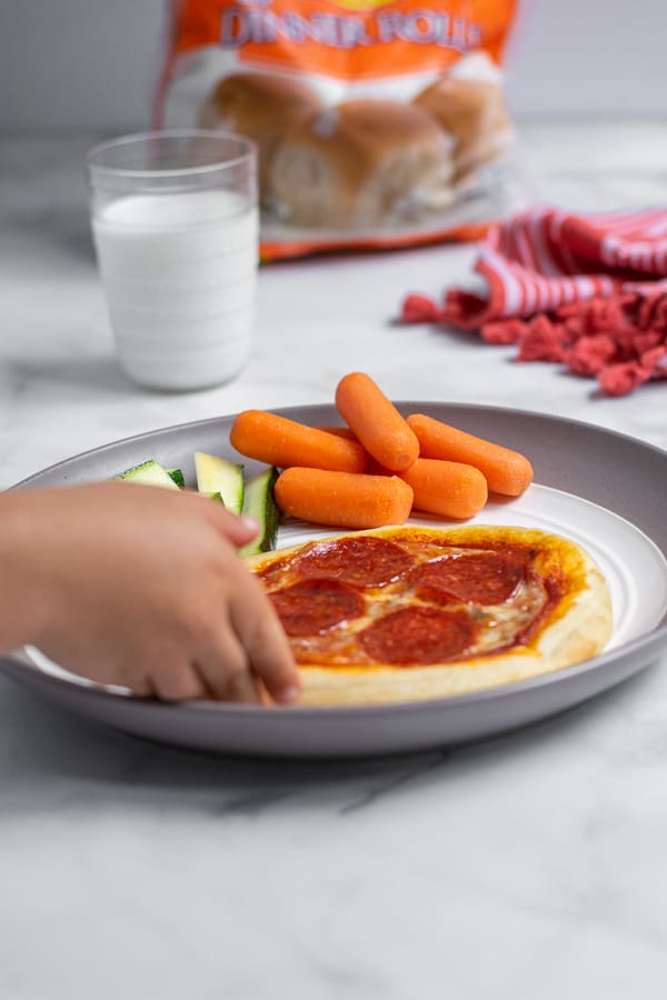 kid hand reaching for a personal pizza off a plate