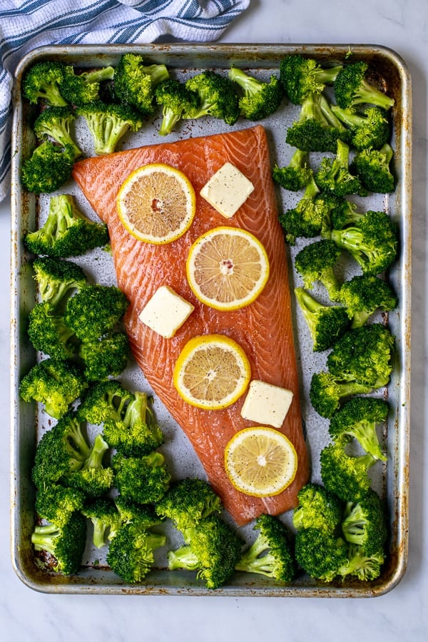 overhead view of raw broccoli and salmon on a sheet pan ready for the oven