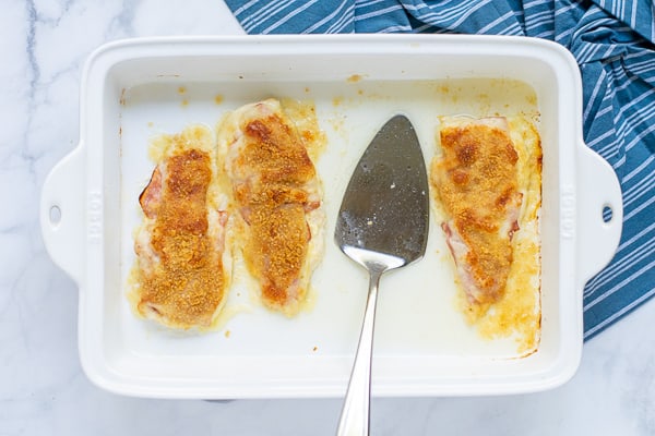3 chicken cordon bleu in a baking dish with a serving utensil