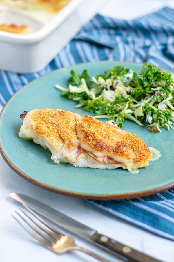 a chicken cordon bleu chicken breast sitting on a teal plate with a side salad