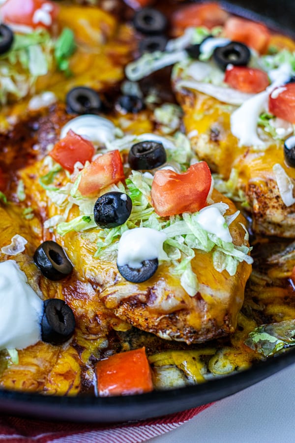 close up of skillet taco chicken breast in a pan covered in taco toppings