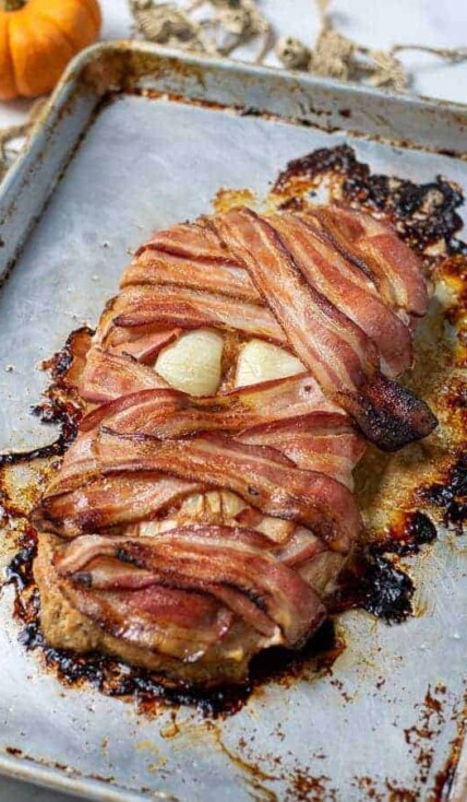bacon wrapped meatloaf mummy on a sheet pan perfect for halloween dinner