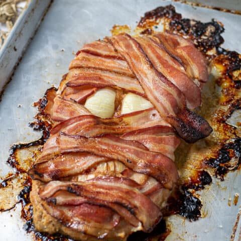 bacon wrapped meatloaf mummy on a sheet pan perfect for halloween dinner