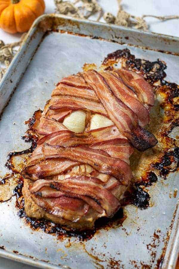 bacon wrapped meatloaf mummy on a sheet pan perfect for halloween dinner
