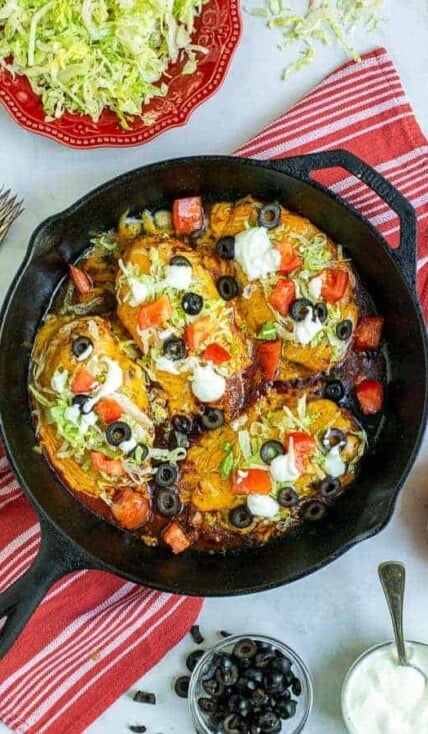 Taco Chicken Breasts in a cast iron skillet with lettuce, tomatoes, sour cream, and black olives