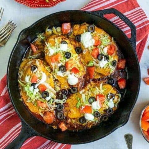 Taco Chicken Breasts in a cast iron skillet with lettuce, tomatoes, sour cream, and black olives