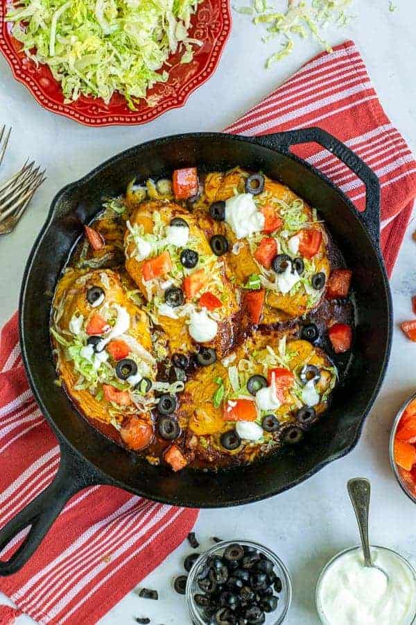 Taco Chicken Breasts in a cast iron skillet with lettuce, tomatoes, sour cream, and black olives