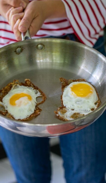 person holding a stainless steel frying pan with 2 fried eggs in it