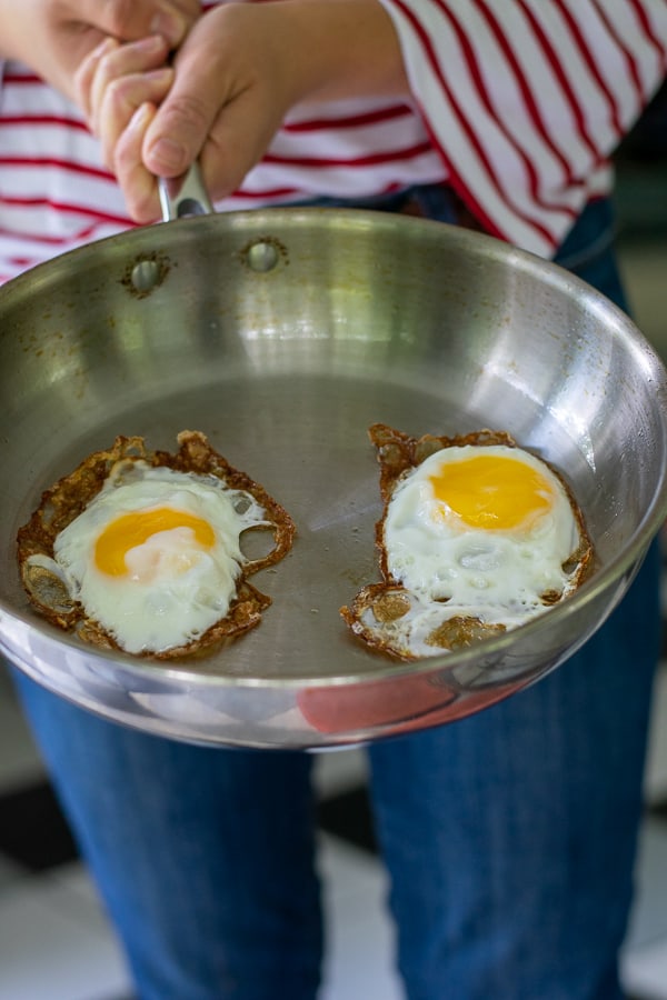 person holding a stainless steel frying pan with 2 fried eggs in it