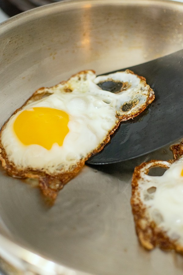 spatula under a fried egg in a frying pan