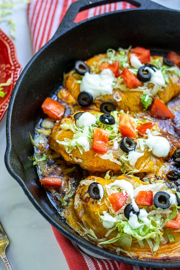 three taco chicken breasts in a skillet covered in lettuce, cheese, tomatoes, and sour cream
