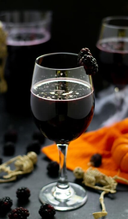 blackberry halloween sangria in a wine glass with fruit and pumpkins and skeletons on the table