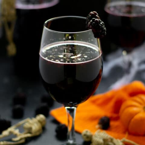 blackberry halloween sangria in a wine glass with fruit and pumpkins and skeletons on the table
