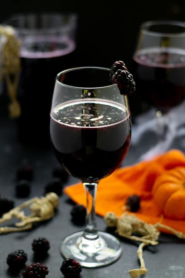blackberry halloween sangria in a wine glass with fruit and pumpkins and skeletons on the table