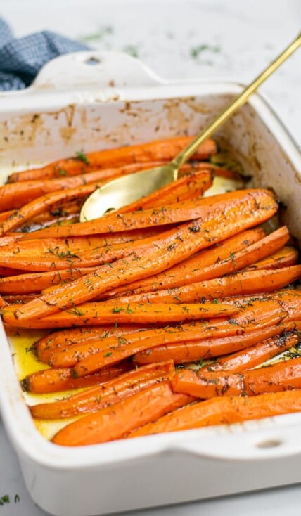 roasted carrots with dill and brown sugar in a white baking dish with a gold spoon