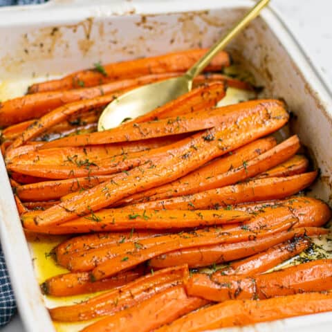 roasted carrots with dill and brown sugar in a white baking dish with a gold spoon
