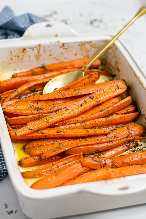 roasted carrots with dill and brown sugar in a white baking dish with a gold spoon