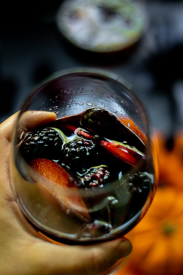 hand holding a glass full of fruits and black halloween sangria