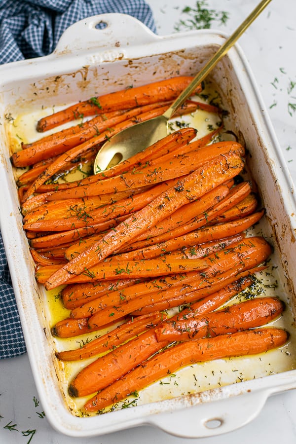 spoon in the white baking dish filled with roasted carrots