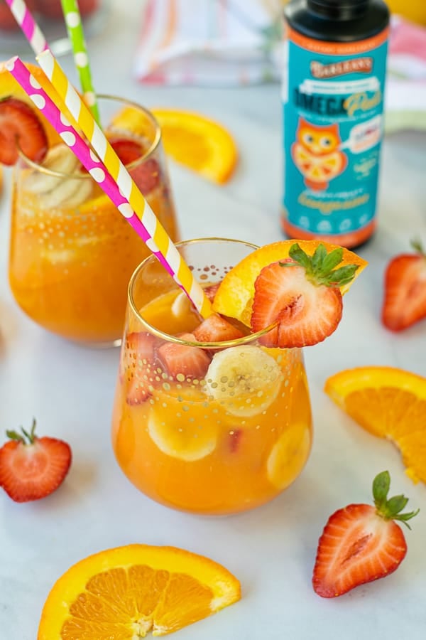 Breakfast orange juice mocktail in a glass with paper straws and colorful fruit