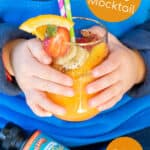 young child holding a glass of orange juice mocktail