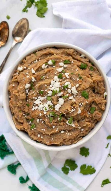 recipe for refried beans made in the instant pot in a white bowl with cilantro