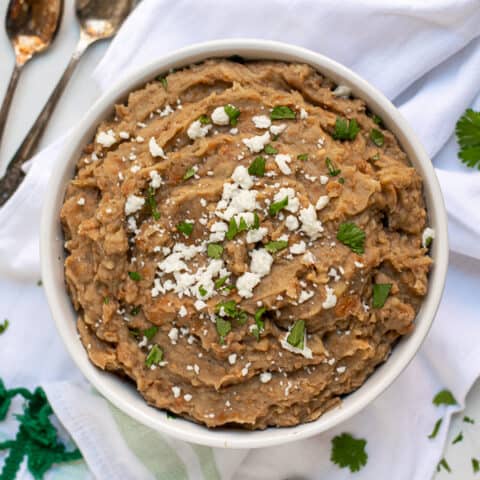 recipe for refried beans made in the instant pot in a white bowl with cilantro