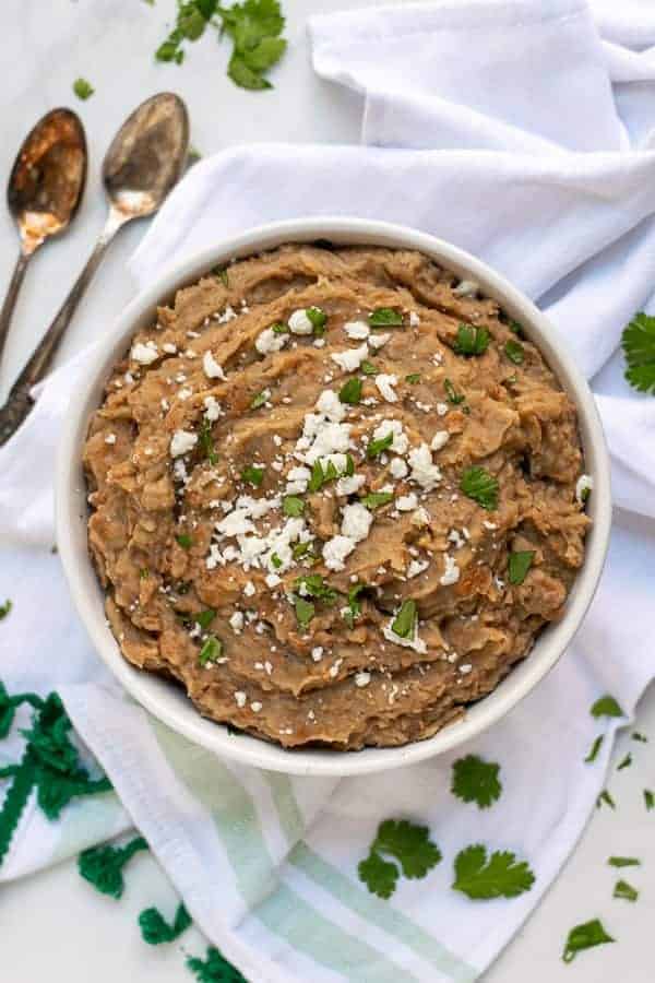 recipe for refried beans made in the instant pot in a white bowl with cilantro