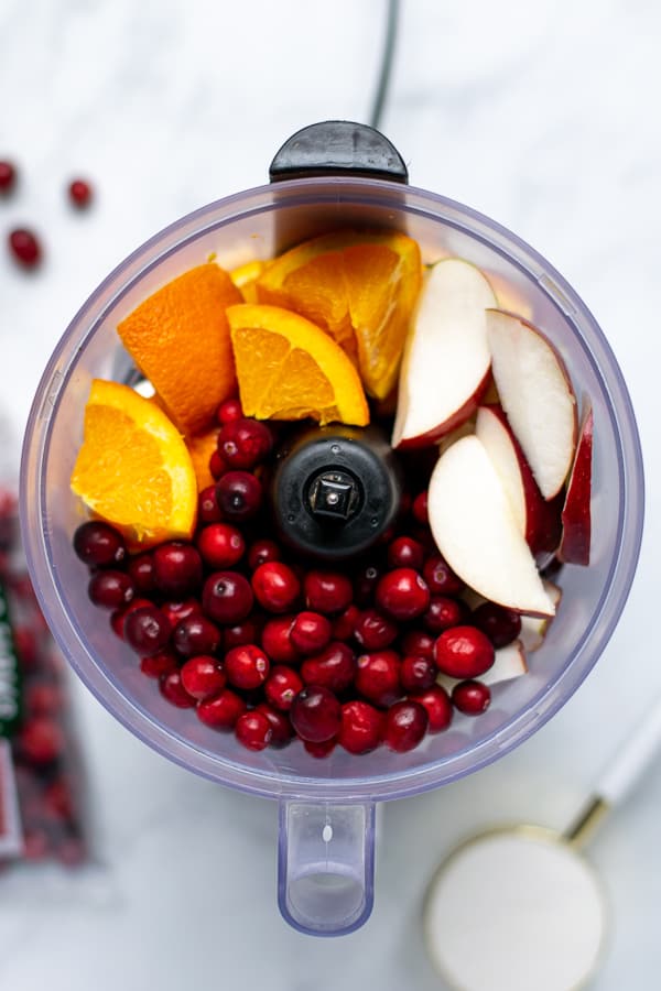 food processor with oranges, apples, and raw cranberries