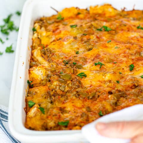 hands with towels holding a white baking dish filled with fresh tex-mex egg bake