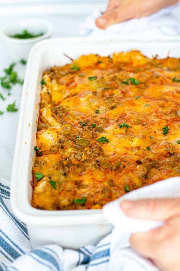 hands with towels holding a white baking dish filled with fresh tex-mex egg bake