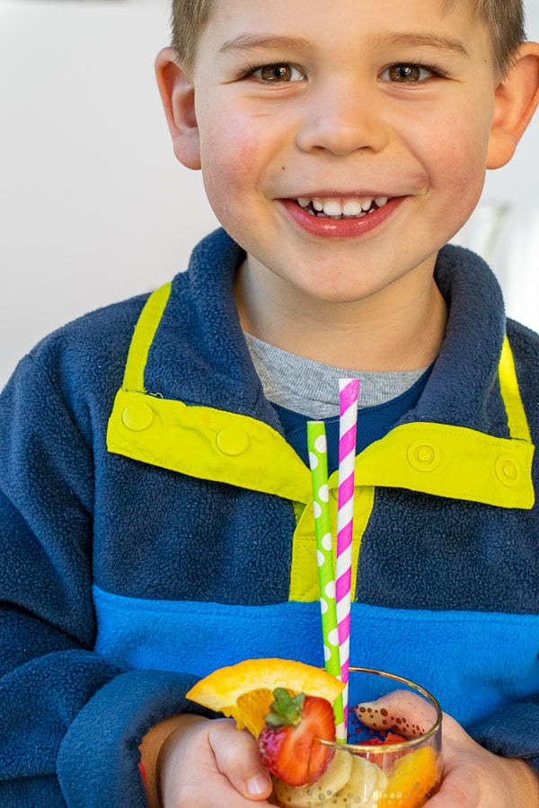 kid smiling holding a glass of orange juice mocktail