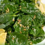 nuts and cheese garnish a spinach salad on a white platter