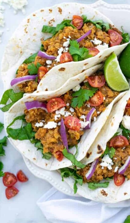 three red lentil tacos with vegetarian taco meat on a white plate with garnishes