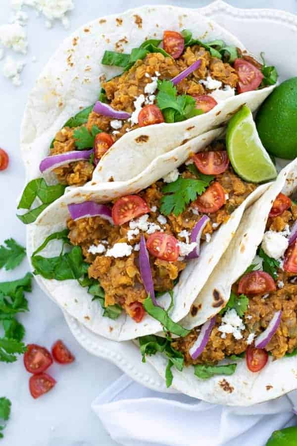 three red lentil tacos with vegetarian taco meat on a white plate with garnishes