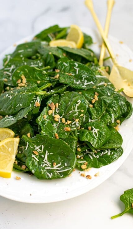 a white platter full of simple spinach salad with cheese and walnuts