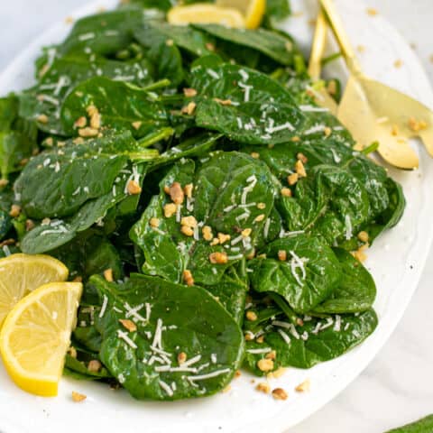 a white platter full of simple spinach salad with cheese and walnuts