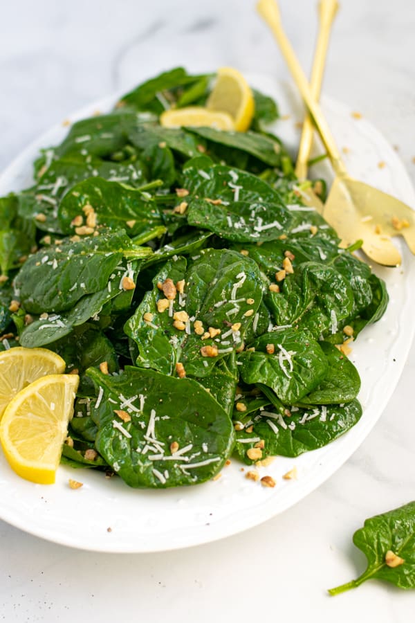 a white platter full of simple spinach salad with cheese and walnuts