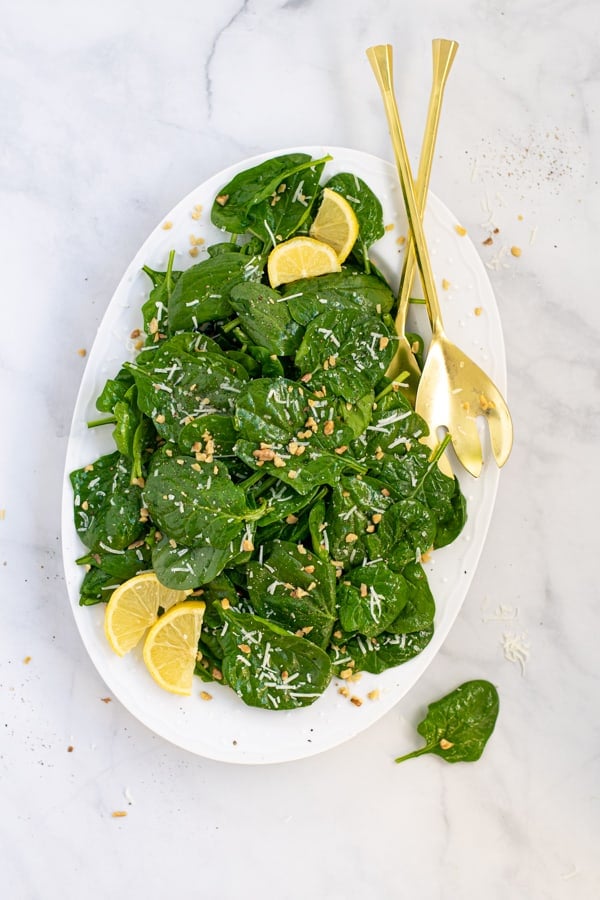 simple spinach salad on a white platter garnished with lemon wedges