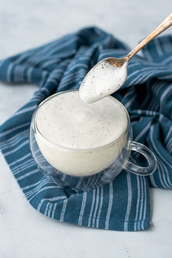 milk foam on a spoon hovering over a mug filled to the brim with milk steamer and foam