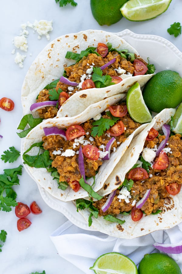 three red lentil tacos sit-in non a white plate with colorful garnishes