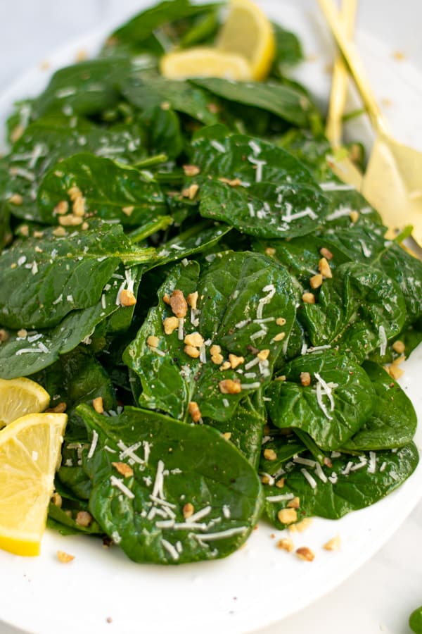 spinach salad on a white platter with lemon wedges, cheese, and nuts