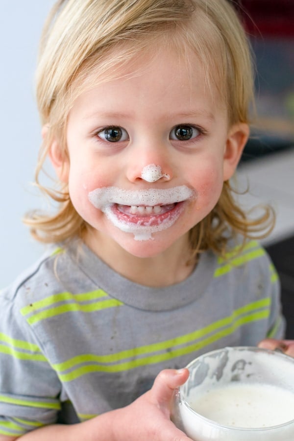 toddler smiling with a steamer in his hand and milk foam all over his mouth and nose