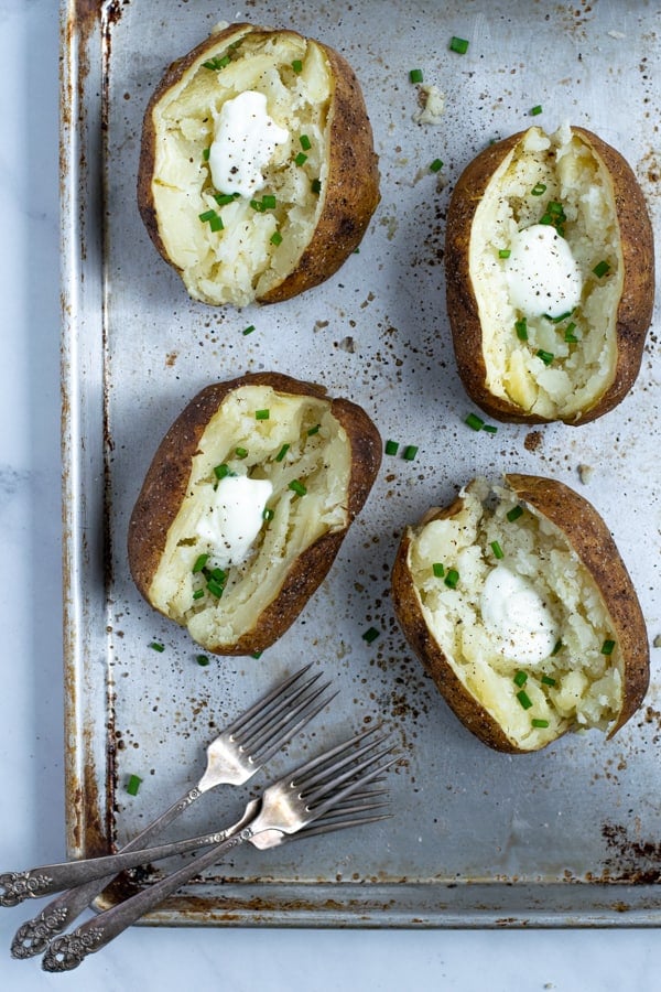 baked potatoes in a tray slices open with sour cream and chives