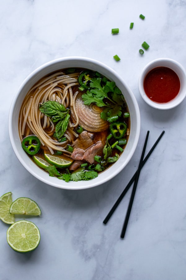 bowl of beef pho in a large bowl with green garnishes
