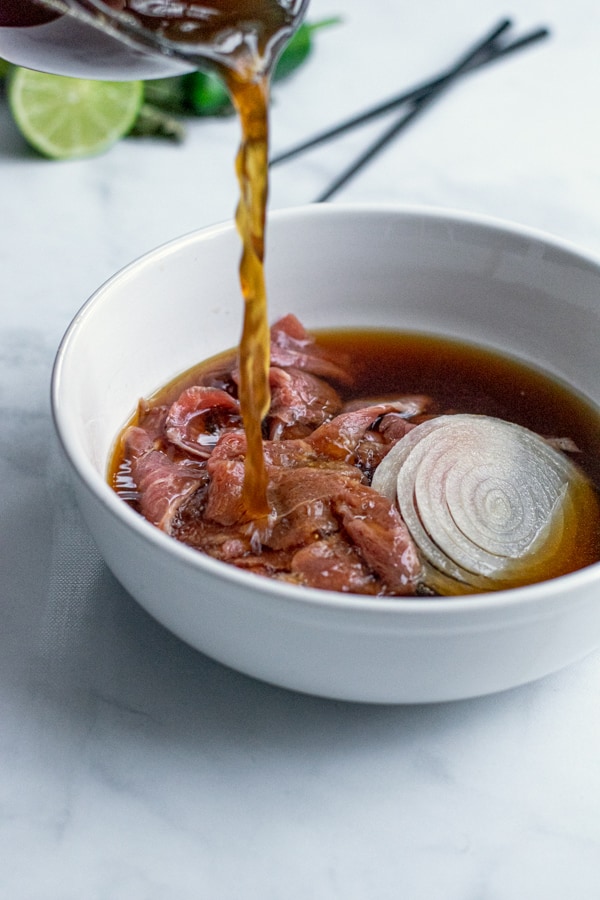 pho broth being poured over top steak and sliced onions