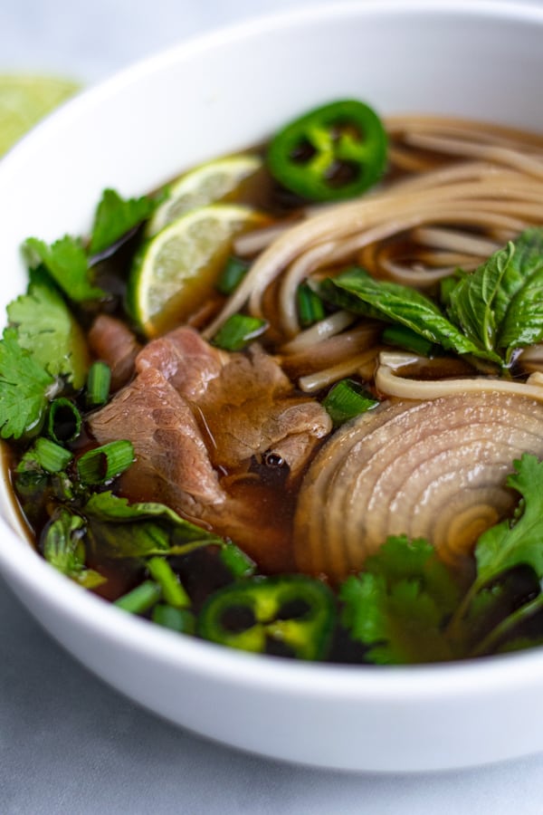 close up of steak, noodles, and garnishes in broth