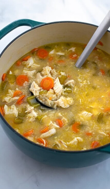 blue dutch oven filled with chicken and rice soup with a ladle full of soup