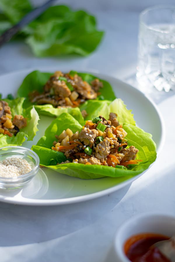 a white plate full of asian chicken lettuce wraps with sesame seeds and green onions