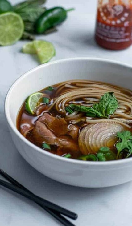 bowl of beef pho made in the slow cooker covered in green garnishes are ready to eat